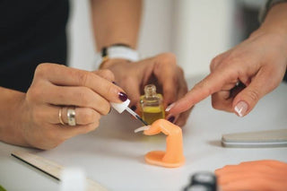 Nail technician practicing a manicure on a realistic silicone nail practice hand.